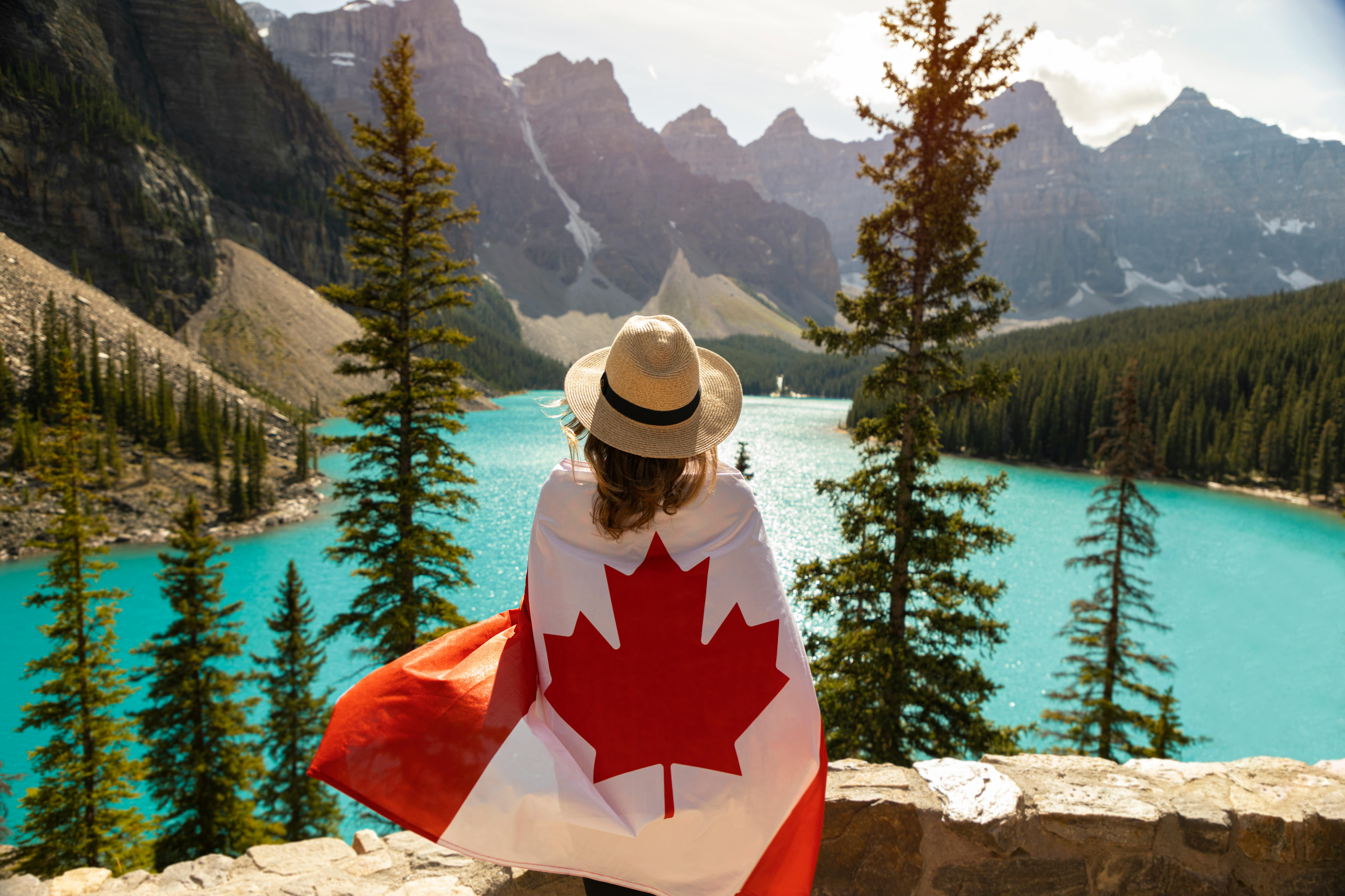 Mujer feliz con la bandera canadiense en la naturaleza después de lograr un trabajo en Canadá.