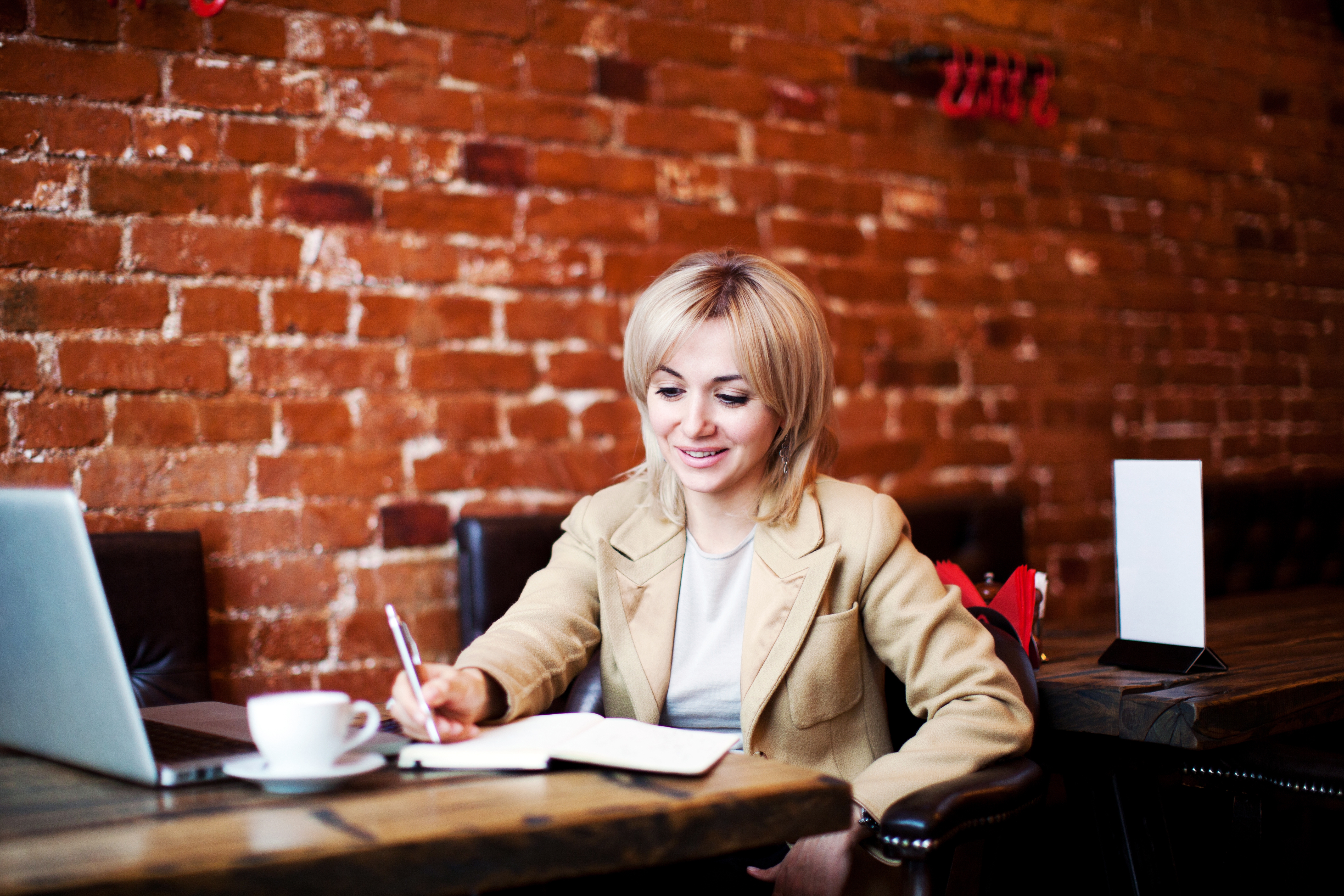 Mujer escribiendo mientras aprende algo desde su computadora.