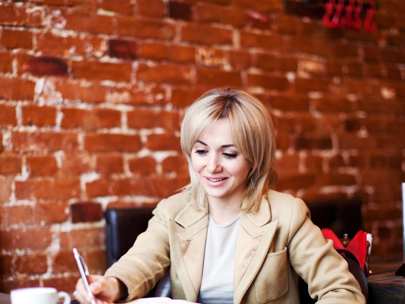 Mujer escribiendo mientras aprende algo desde su computadora.