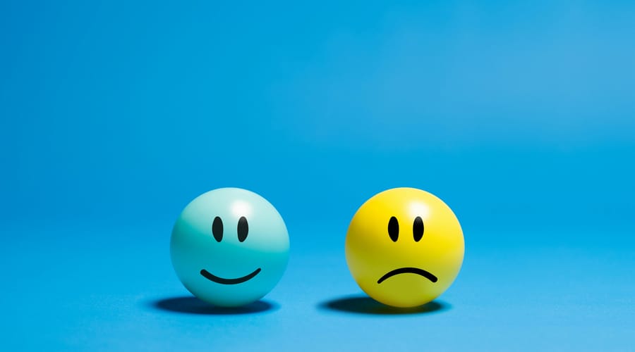 Dos esferas con expresiones opuestas: una feliz y otra triste sobre un fondo azul para representar la inteligencia emocional.