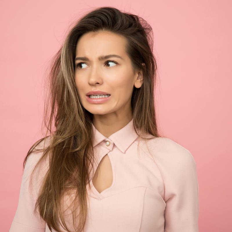 Mujer con cara de preocupación por olvidar su idioma natal. Fondo rosa.