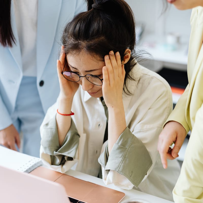 Mujer con dolor de cabeza en el trabajo por sentir presión social por no hablar inglés.