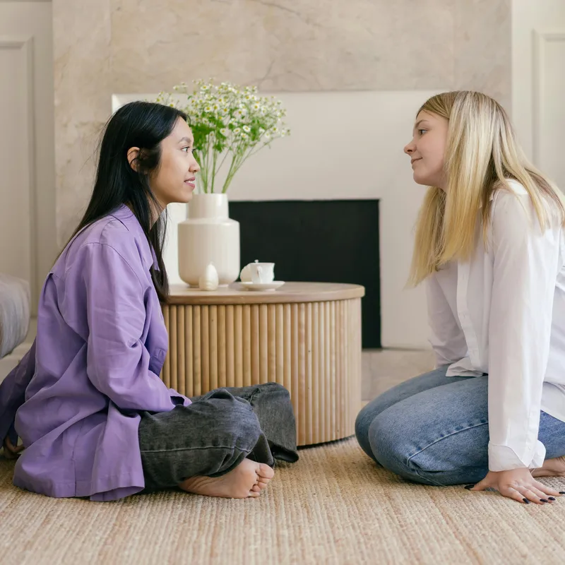 Dos amigas sentadas en el piso haciendo comentarios en inglés.
