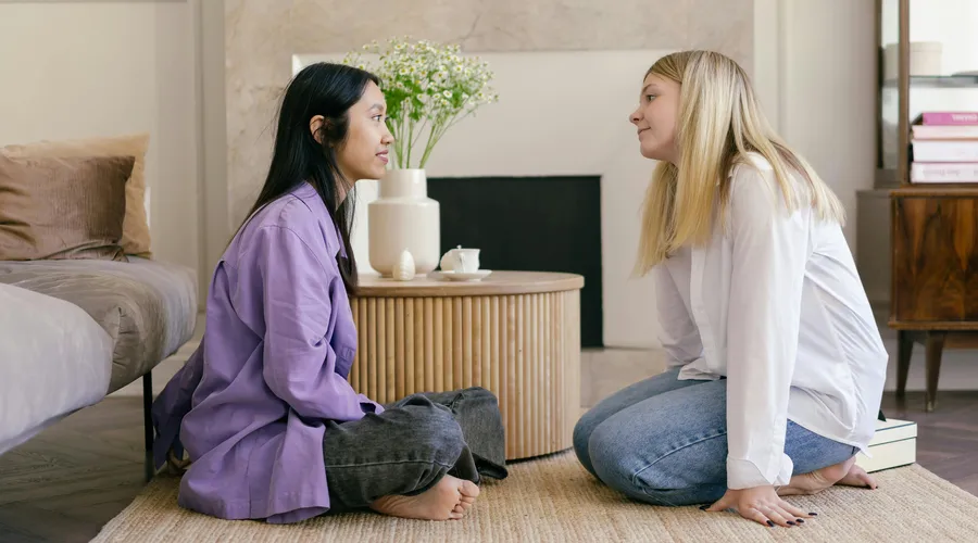 Dos amigas sentadas en el piso haciendo comentarios en inglés.