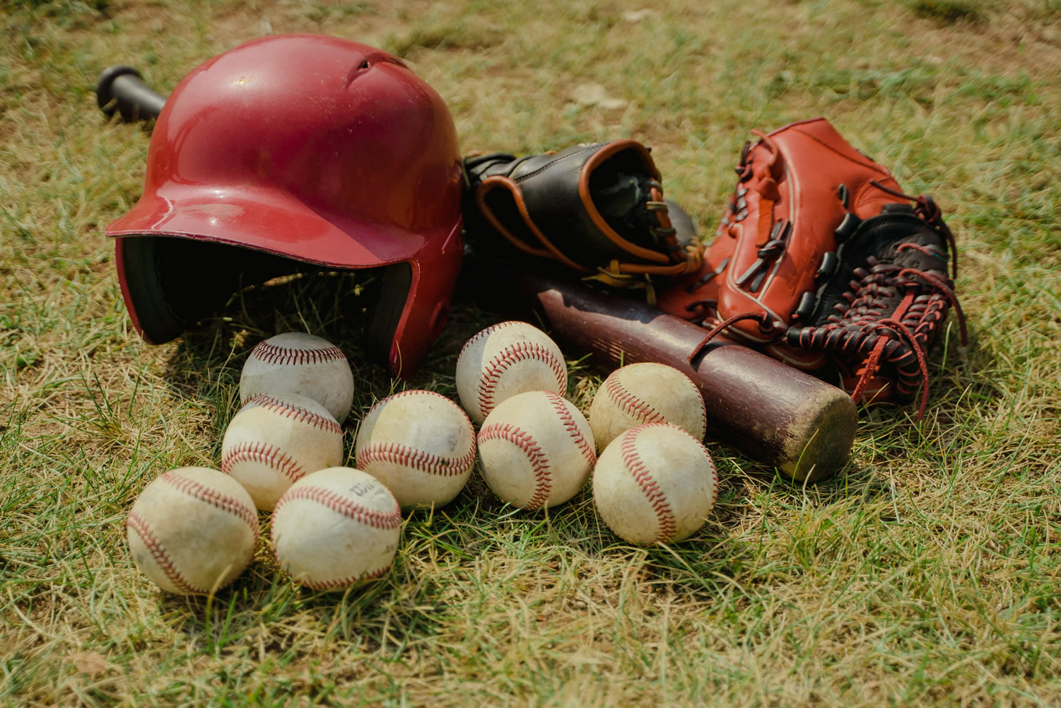 Casco, bat, manoplas y pelotas de béisbol en el campo