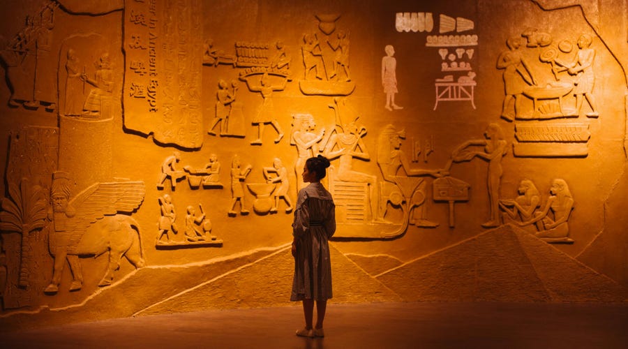 Una mujer visita un museo egipcio, uno de los idiomas antiguos, con escritos e imágenes en la pared.